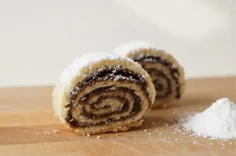 עוגיות מגולגלות תמרים מבצק פריך נימוח עם אבקת סוכר, מתכון למגולגלות תמרים פרווה שנמסות בפה לצד קפה, צילום תקריב מקצועי של עוגיות תמרים של פעם.