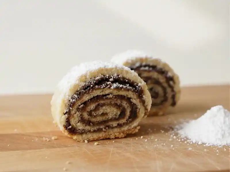 עוגיות מגולגלות תמרים מבצק פריך נימוח עם אבקת סוכר, מתכון למגולגלות תמרים פרווה שנמסות בפה לצד קפה, צילום תקריב מקצועי של עוגיות תמרים של פעם.